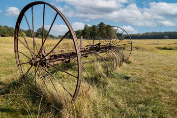 An old hay mower standing in a field under a blue sky
