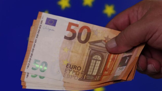 Counting 50 Euro notes in front of the European Union flag during the day