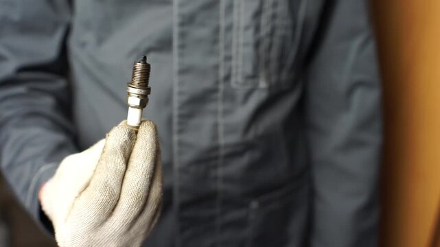 A mechanic shows old spark plugs. Defective spark plugs covered in motor oil and soot. Replacing spark plugs.