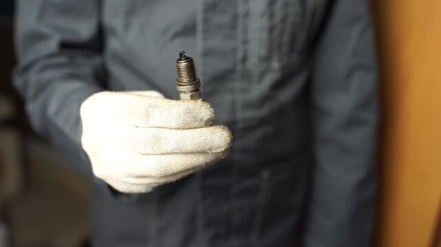 A mechanic shows old spark plugs. Defective spark plugs covered in motor oil and soot. Replacing spark plugs.