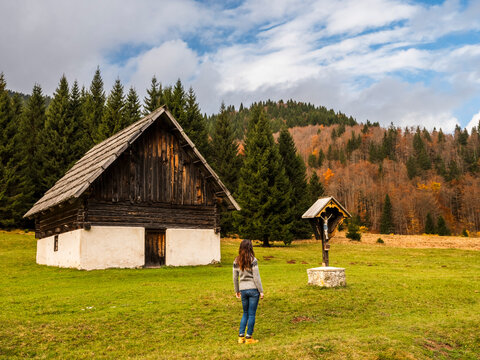 A woman stands in a field looking at a wooden building and a crucifix. Bartolo Valley,Tarvisio,Friuli Venezia Giulia,Italy