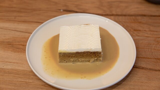 Milk cake a khaliji dessert on a white ceramic plate resting on a wooden table in a rustic style cafe
