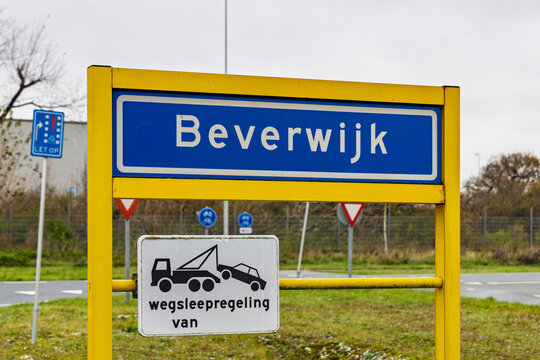A blue city entrance sign for Beverwijk, Netherlands, featuring a yellow frame and a towing zone warning sign against a blurred background.