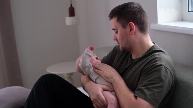 A father comforts his crying little son. A man cradles his newborn in his arms. The concept of active fatherhood and love for the baby.