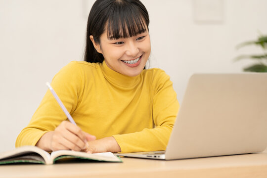 Smiling young Asian woman studying online with laptop and book at home, online learning and education concept, remote study lifestyle. student, study, studying, online, learning, education, laptop.