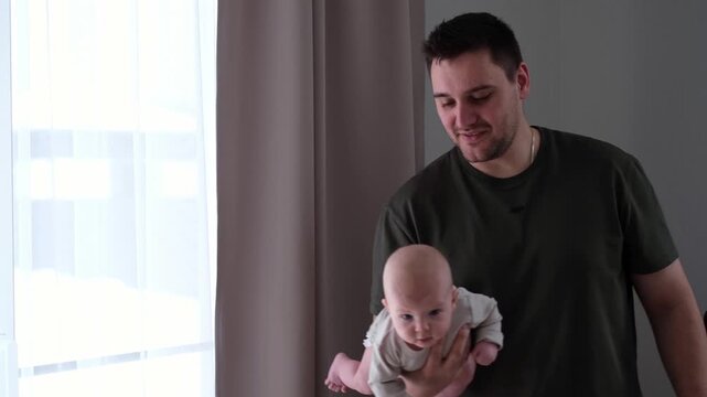The middle plan of the portrait is in warm colors of a young father and newborn son. A father plays and kisses his little son on the bed. The concept of love, happy fatherhood.