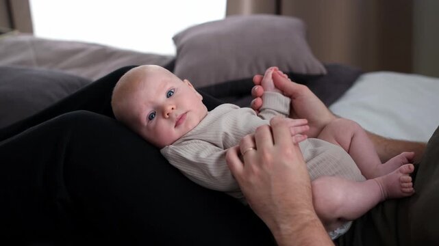 The middle plan of the portrait is in warm colors of a young father and newborn son. A father plays and kisses his little son on the bed. The concept of love, happy fatherhood.