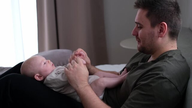 The middle plan of the portrait is in warm colors of a young father and newborn son. A father plays and kisses his little son on the bed. The concept of love, happy fatherhood.