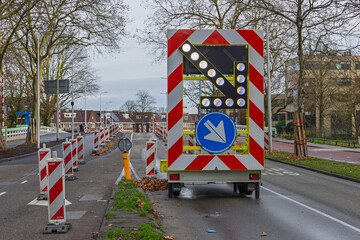 Mobile traffic warning trailer with an illuminated LED arrow and chevron patterns directing traffic during road construction in the Netherlands.