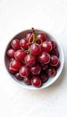 Obraz premium Ripe red grapes are in a white bowl. The fruit looks fresh and healthy. Simple composition with clean white background. Good for food related projects.