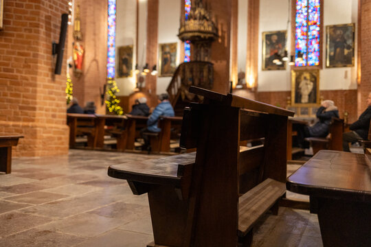 Catholic church interior with empty wooden pews in the foreground and only a few worshippers in the background. Visual symbol of declining church attendance, secularization, and reduced participation 