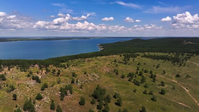 Aerial footage of scenic mountain slopes and a vast lake in the Borovoe resort area. Rocky hills, pine forests, and the deep blue water create a sense of space, calm.