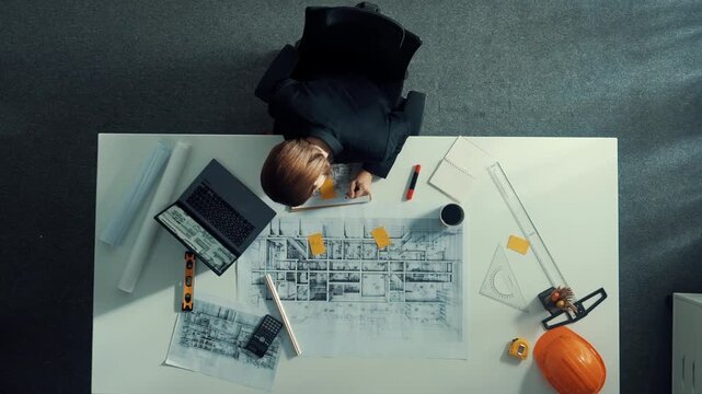 Time lapse of smart architect drawing while working at laptop. Top down view of caucasian engineer designing blueprint and drafting house model at table with equipment and safety helmet. Alimentation.