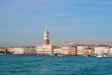 Obraz premium Venice Skyline with St Mark’s Campanile and Grand Canal - Panoramic view of Venice skyline with St Mark’s Campanile, historic buildings, and boats on the water under a clear blue sky in Italy. 