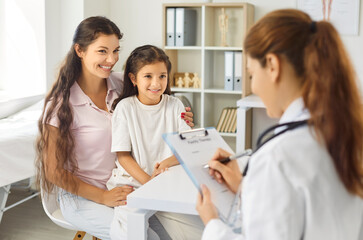 Obraz premium Pediatrician counsels mother and daughter during session. The clinician writes on a clipboard in the clinic. Smiles suggest trust and comfort. Concept family counseling with support and care.