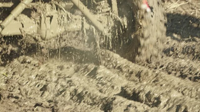 A close-up of a racing SUV. Dirty, spinning wheels and suspension kicking up mud. An energetic, brutal, and powerful atmosphere. Rear view. Slow motion