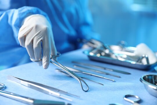 Doctor with different surgical tools at table in hospital, closeup