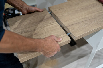 Man's hands installing a wooden panel into furniture using metal dowels, indicating diy assembly and home renovation