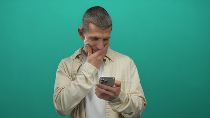 Caucasian man engaging with smartphone against isolated green background wall, highlighting...