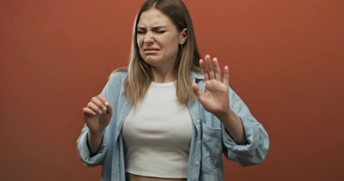 Young Woman Expressing Intense Disgust and Repulsion, Averse Emotional Reaction in Studio Against Orange Background, 4K