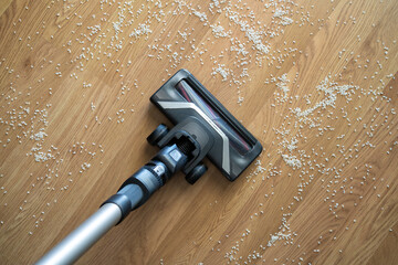 Vacuum cleaner nozzle sucking up spilled rice grains from an oak parquet floor, showing home cleaning and house chores