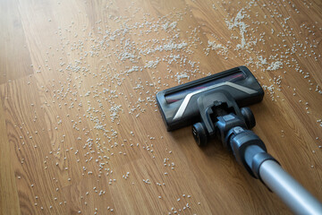Vacuum cleaner nozzle sucking up spilled rice grains from an oak parquet floor, showing home cleaning and house chores