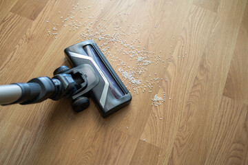 Vacuum cleaner nozzle sucking up spilled rice grains from an oak parquet floor, showing home cleaning and house chores
