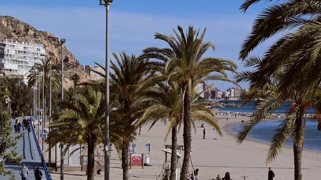 Visitors walk along the waterfront promenade near Parque de Calistenia del Postiguet in Alicante, Spain on a sunny day