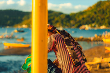 a person with his face hidden from a yellow pole by the beach