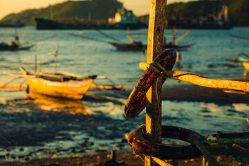 a boat fender hanging on wooden fence with philippine boats in the background during sunrise near the beach