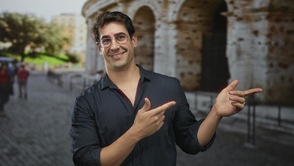 Fototapeta premium Man pointing with fingers and smiling in front of historic building on a street; playful confidence.