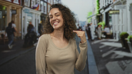 Young hispanic woman smiling with face centered on a busy city street, looking at camera in daylight; everyday happiness.