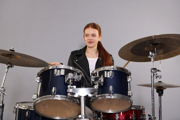Teenage girl with drumsticks and drums on light grey background