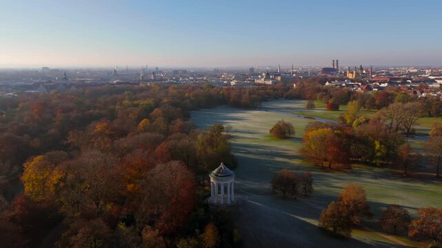 Aerial drone view over Englischer Garten in Munich on cold autumn morning. Scene shows Monopteros, frosty meadows and skyline with Frauenkirche, Theatinerkirche and the Bavarian State Chancellery
