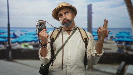 Obraz premium Man holding vintage camera in hand with backpack on street near beach promenade; melancholy travel nostalgia.
