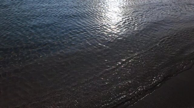 View of ta vertical footage of calm small waves next to the sandy Manganari beach in Ios Greece while the sun is slowly setting in slow motion