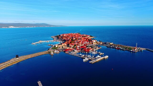 Small historic town located on a narrow peninsula connected by a road to the mainland. Blue water surrounds the island-like landmass. Clear sky. Aerial view.