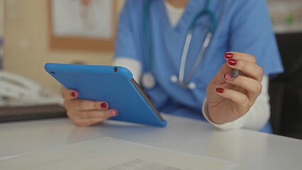 Fototapeta premium Woman in scrubs uses tablet with stylus in clinic setting, emphasizing indoor healthcare workplace environment and focus on technology, communication, and modern medical practices.
