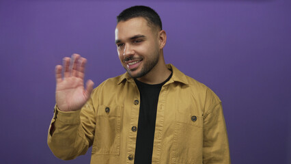 Fototapeta premium Man wearing mustard shirt and black tee with trimmed beard waving hand and smiling broadly in studio; joy.