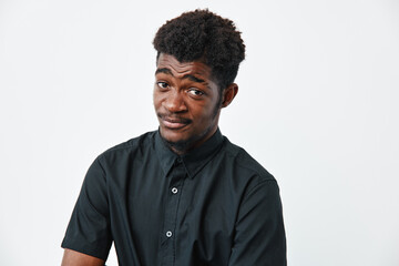 Obraz premium Young black man with dark skin wearing black shirt posing with skeptical expression on white background. African ethnicity, casual style and confident attitude in studio portrait.