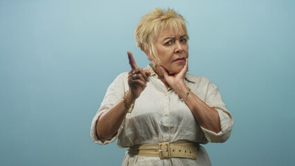 Fototapeta premium Senior woman pointing finger and touching chin in studio portrait, expressive hand gestures and portrait pose; thoughtful contemplation.