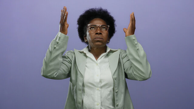 Woman feeling stressed with hands over face against isolated purple background wearing glasses in a green coat looking upward in concern.