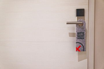 Do not disturb tag in german language on metal handle of white hotel door.