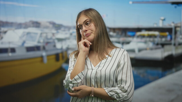 Woman shrugs with both hands open beside a docked boat at a sunny port; uncertainty hesitation doubt.