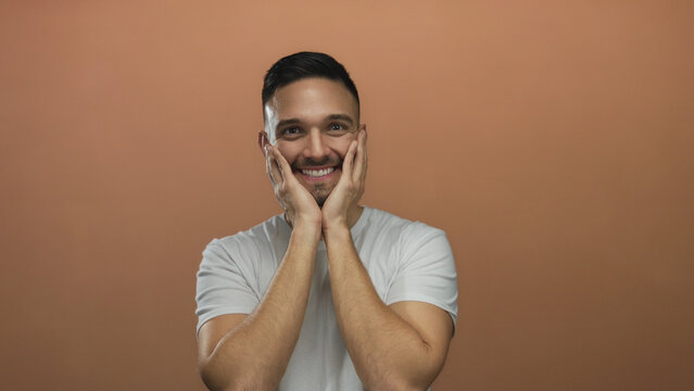 Hispanic young man in casual white shirt with short hair smiling against orange background conveying positivity and energy