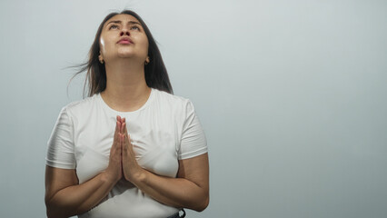 Obraz premium Woman with hands pressed together in prayer, eyes raised and bare hands visible in a light gray studio setting; hope devotion.