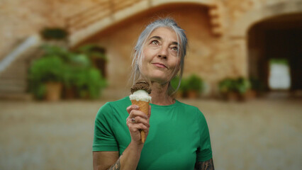 Fototapeta premium Woman enjoying ice cream outdoors at old university, showcasing the serene moment of a senior lady in a casual setting with historic charm in the background.