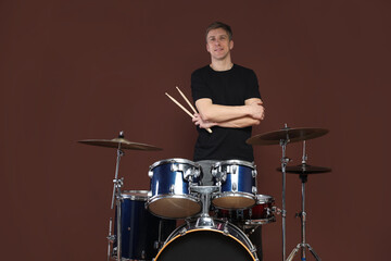 Smiling man with drumsticks and drum kit on brown background