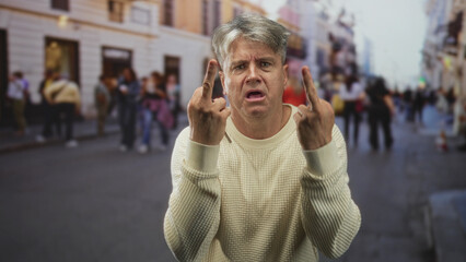 Fototapeta premium Man showing middle fingers and holding car keys on a crowded street, grey hair and cream sweater visible; frustration.