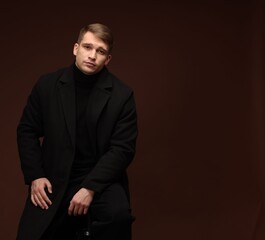 Fototapeta premium Fashion model. Portrait of handsome man posing against dark brown background, space for text